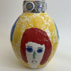 ceramic vase mainly decorated with white and yellow sgraffito, featuring a large human face with red hair and slightly raised green nose. 