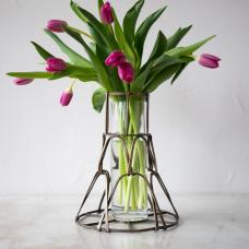 This basket vase features a woven design made from forged brass. It can be used to elevate a bouquet of fresh flowers  or simply as a one-of-a-kind artistic piece. A glass cylinder is also included. Shown in antique brass patina.