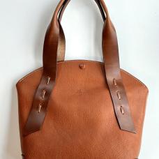 The Arc Tote bag is a contrast of textures and shapes combined with repeating arcs. Hand-sewn with waxed thread and saddle-stitching technique  the ribbon-like handles are attached with large laced stitches. Features brass feet  an inside pocket  a reinforced bottom and a covered snap closure.